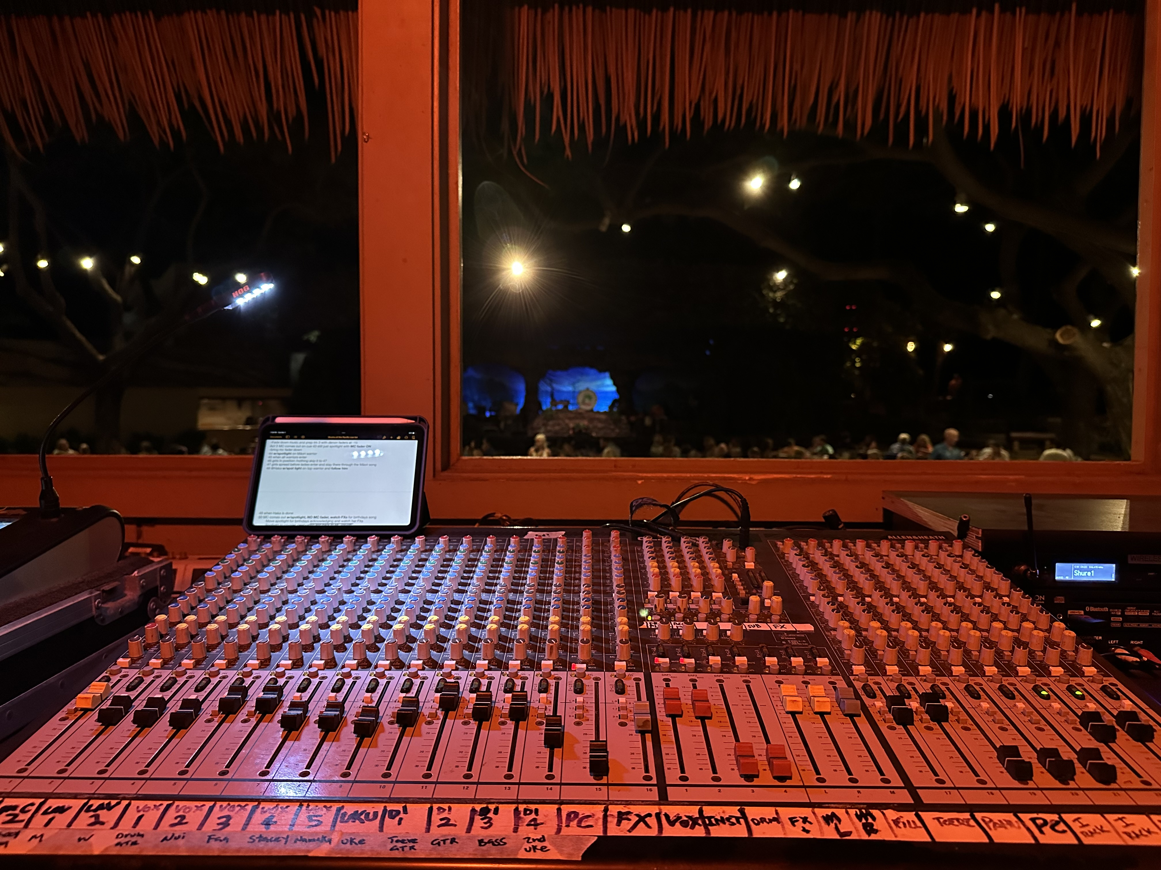 Analog audio mixer board with rows of knobs and meters in a dim production room